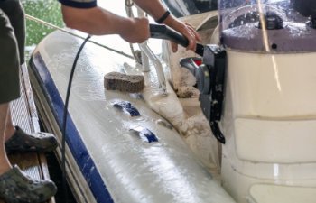 man washing white inflatable boat with brush and pressure water system
