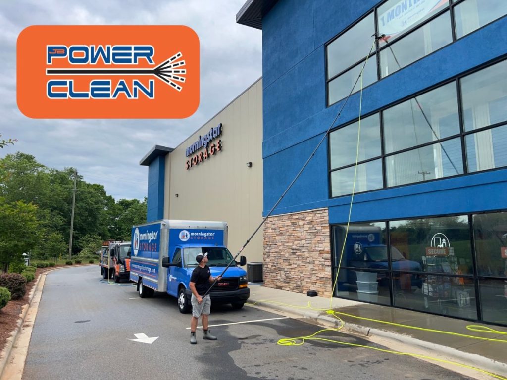 JB Power Clean technician washing windows at Morningstar Storage building using a water-fed pole system; branded service vehicle visible in foreground